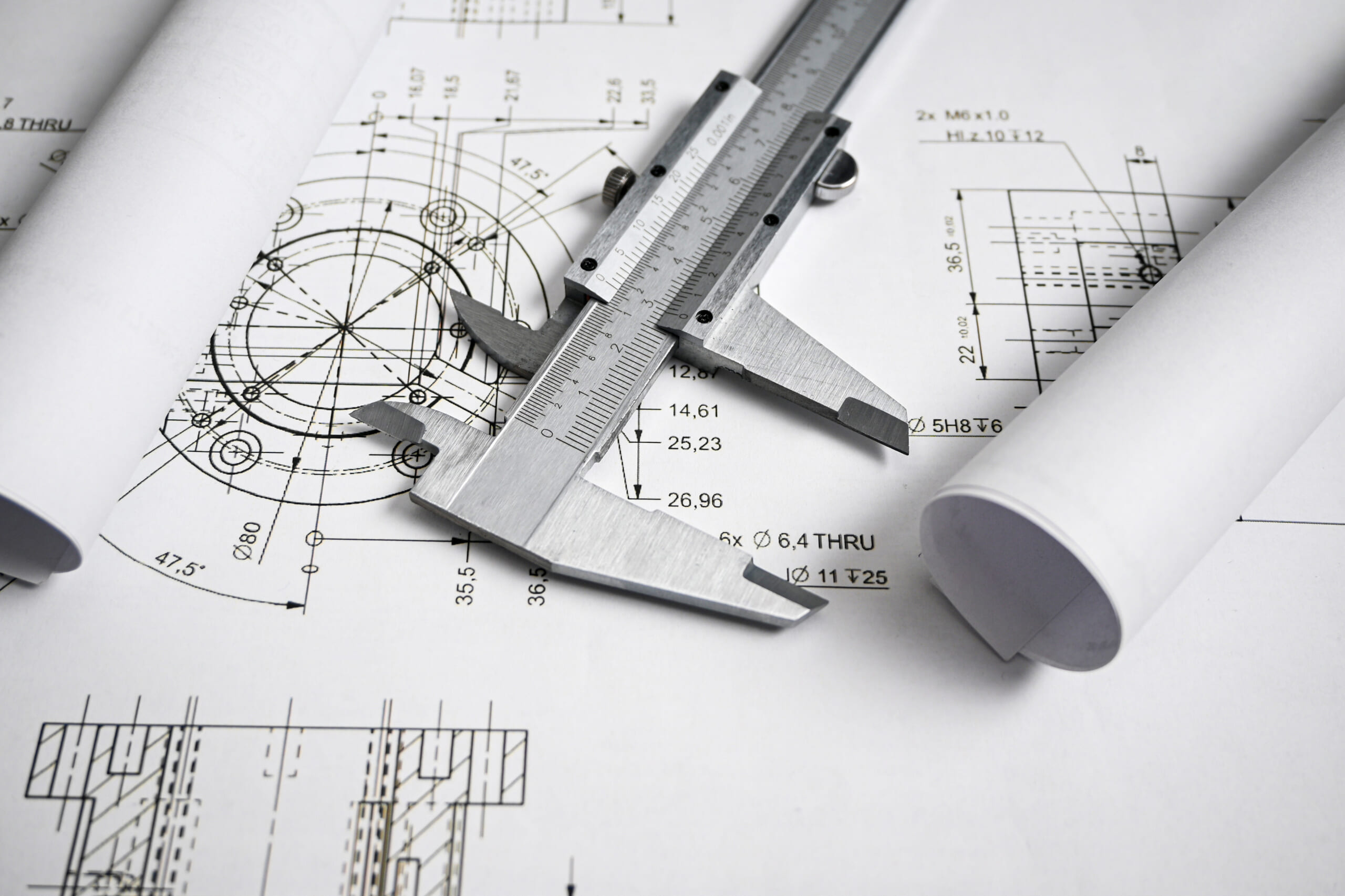 Caliper rests on rolled blueprints, highlighting the importance of precise measurements in engineering and design.